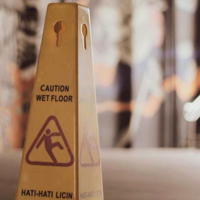 Close-up of a yellow wet floor sign with caution text in an indoor setting.
